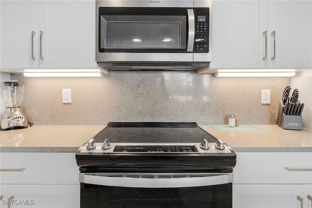 kitchen with decorative backsplash, appliances with stainless steel finishes, white cabinetry, and light stone countertops