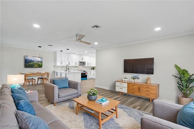 living room featuring crown molding, sink, ceiling fan, and light hardwood / wood-style floors