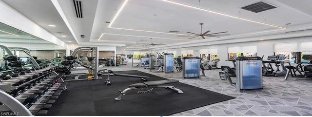 workout area with ceiling fan and a tray ceiling