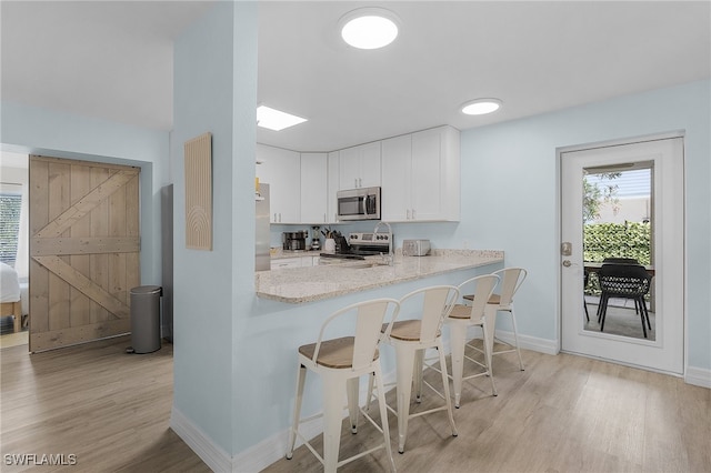 kitchen featuring a kitchen breakfast bar, a barn door, light wood-type flooring, appliances with stainless steel finishes, and white cabinetry