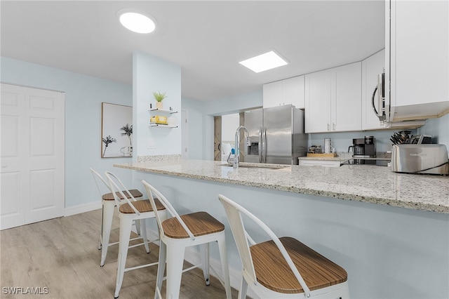 kitchen featuring kitchen peninsula, light stone counters, light wood-type flooring, and appliances with stainless steel finishes