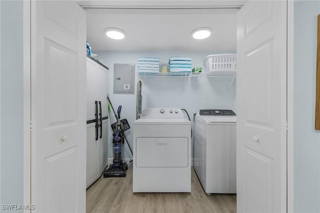 clothes washing area with electric panel, washer and dryer, and light wood-type flooring