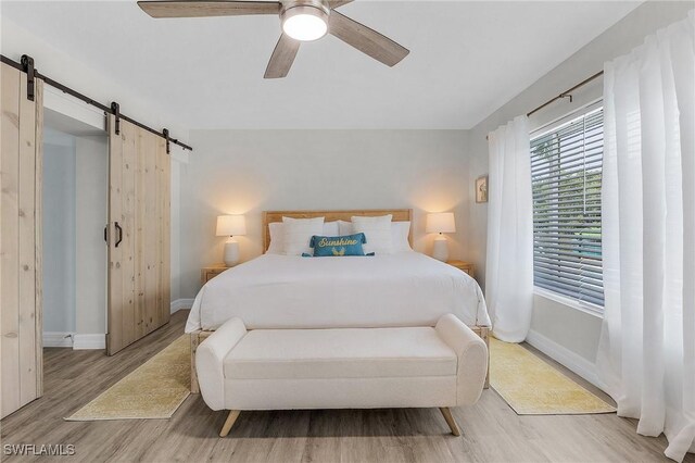 bedroom with a barn door, ceiling fan, and light hardwood / wood-style flooring