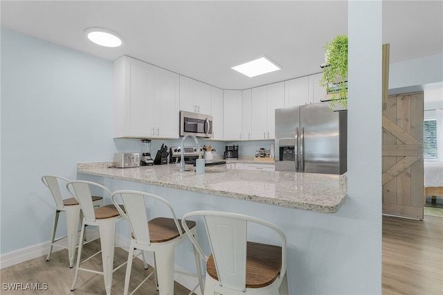 kitchen featuring white cabinets, light wood-type flooring, light stone counters, kitchen peninsula, and stainless steel appliances