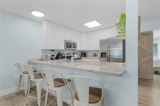 kitchen with white cabinets, stainless steel appliances, light stone countertops, and light wood-type flooring