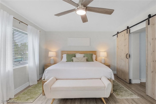 bedroom with ceiling fan, a barn door, and light hardwood / wood-style flooring