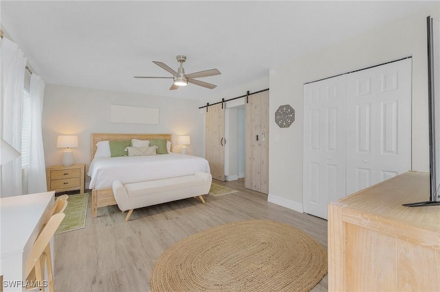 bedroom featuring ceiling fan, a barn door, and light wood-type flooring