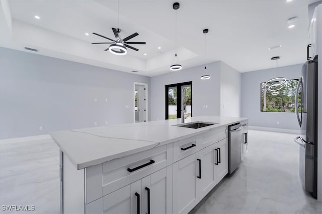 kitchen with light stone countertops, appliances with stainless steel finishes, a raised ceiling, a center island with sink, and white cabinets