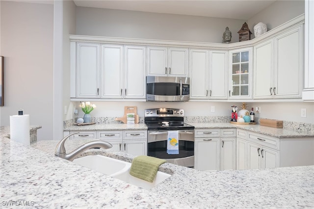 kitchen featuring white cabinets, appliances with stainless steel finishes, light stone countertops, and sink