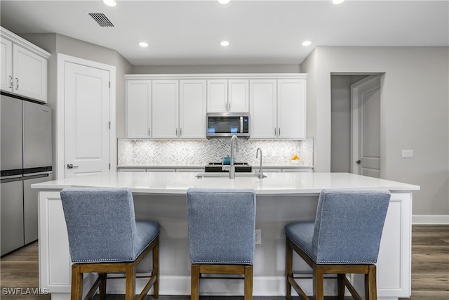 kitchen with white cabinets, an island with sink, dark hardwood / wood-style floors, and appliances with stainless steel finishes