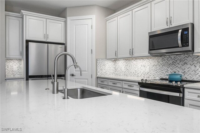 kitchen with decorative backsplash, stainless steel appliances, light stone counters, and sink