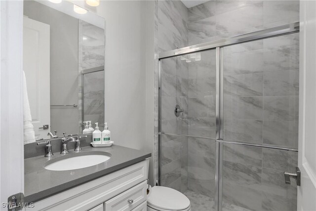 bathroom featuring a shower with door, vanity, and toilet