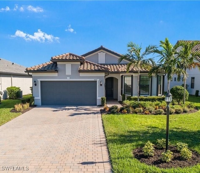 mediterranean / spanish house featuring a garage, a tiled roof, decorative driveway, stucco siding, and a front yard