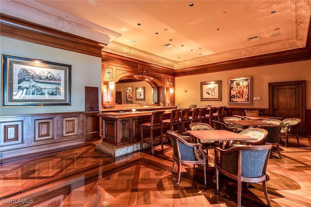 dining room featuring a tray ceiling, bar, ornamental molding, and parquet flooring