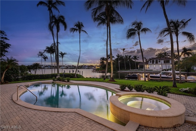 pool at dusk featuring an in ground hot tub and a water view