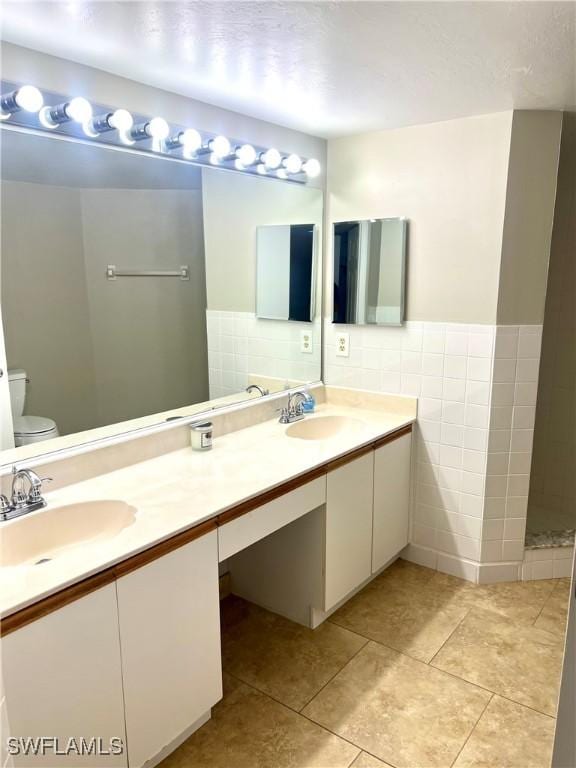 bathroom with a shower, tile walls, tile patterned flooring, vanity, and toilet