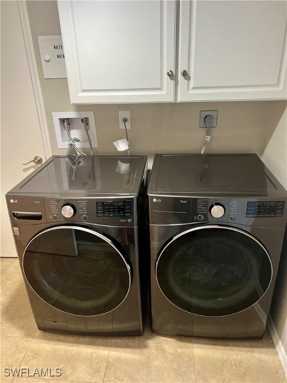 laundry area with cabinets, light tile patterned floors, and washing machine and clothes dryer