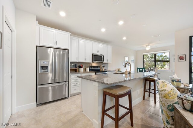 kitchen with light stone countertops, sink, stainless steel appliances, a breakfast bar area, and a kitchen island with sink