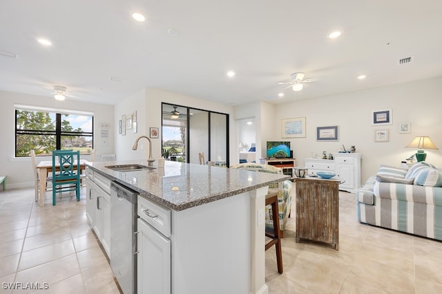 kitchen featuring light stone counters, stainless steel dishwasher, sink, a center island with sink, and white cabinets