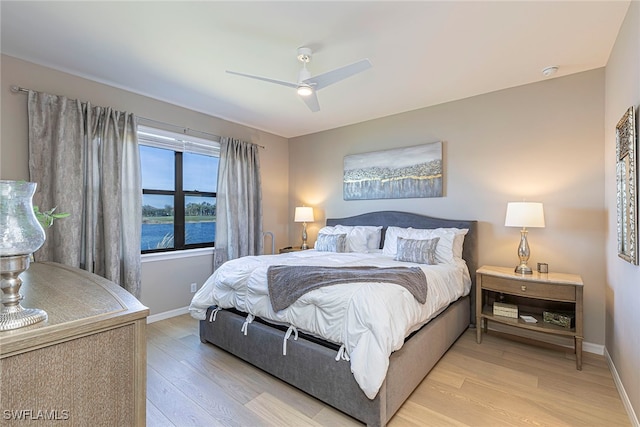 bedroom with ceiling fan, light hardwood / wood-style flooring, and a water view