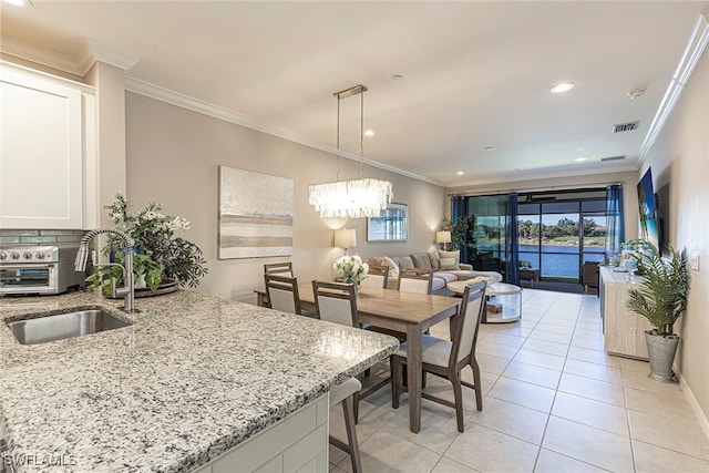 dining space with a notable chandelier, ornamental molding, sink, and light tile patterned floors