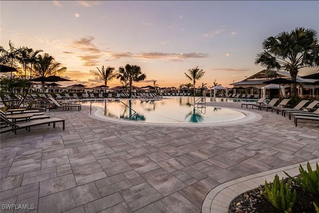 pool at dusk with a patio area and a water view