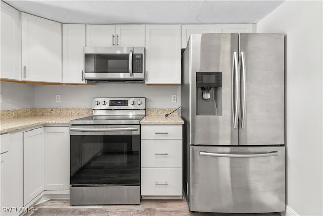 kitchen featuring white cabinets, stainless steel appliances, light stone counters, and light hardwood / wood-style floors