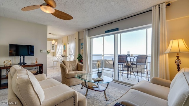 living room featuring a water view, light tile patterned floors, a ceiling fan, and a textured ceiling