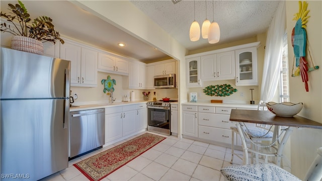 kitchen with a textured ceiling, decorative light fixtures, white cabinetry, and stainless steel appliances