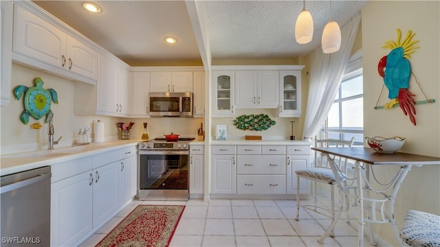 kitchen featuring white cabinets, glass insert cabinets, stainless steel appliances, light countertops, and pendant lighting