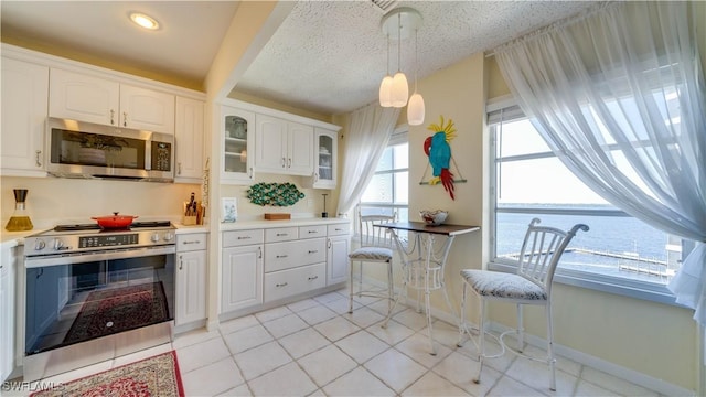 kitchen featuring stainless steel appliances, light countertops, a water view, glass insert cabinets, and white cabinetry