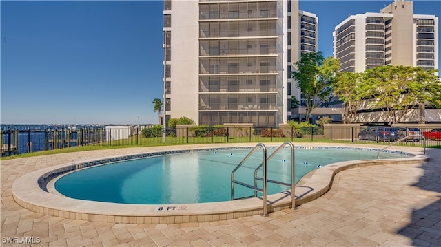 community pool featuring a patio, a water view, and fence