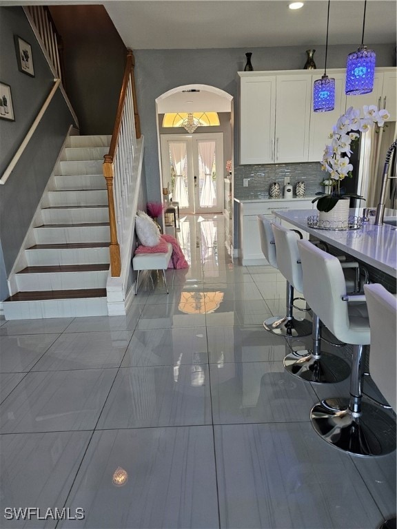 kitchen with white cabinetry, french doors, backsplash, decorative light fixtures, and light tile patterned floors