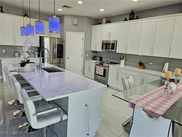 kitchen with pendant lighting, a center island with sink, white cabinets, tasteful backsplash, and stainless steel appliances