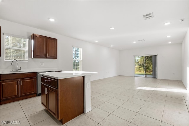 kitchen with light tile patterned flooring, dark brown cabinetry, a kitchen island, and sink