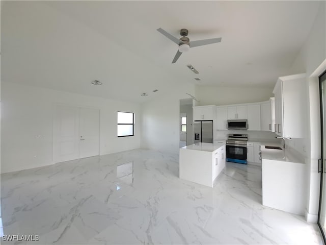 kitchen with lofted ceiling, sink, white cabinetry, stainless steel appliances, and a kitchen island