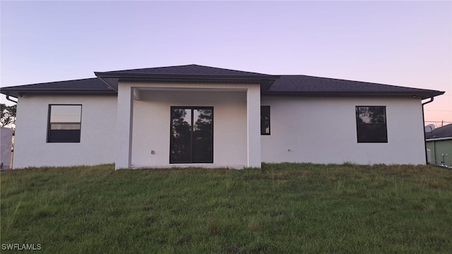 back house at dusk featuring a lawn