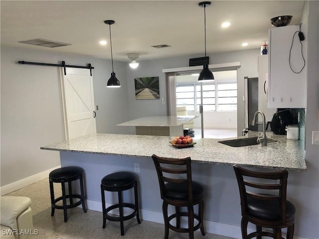 kitchen featuring kitchen peninsula, a barn door, sink, and pendant lighting