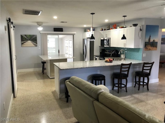 kitchen with appliances with stainless steel finishes, a breakfast bar, pendant lighting, a barn door, and white cabinetry