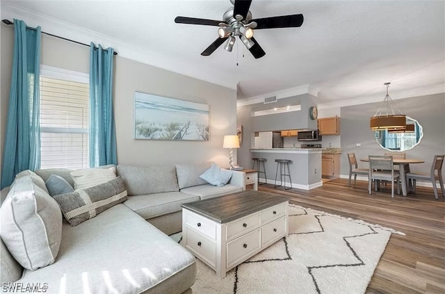 living room with ceiling fan, light wood-type flooring, crown molding, and a wealth of natural light