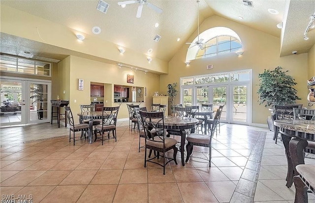 tiled dining space with ceiling fan, a healthy amount of sunlight, high vaulted ceiling, and french doors