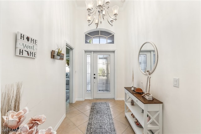 tiled entryway featuring ornamental molding, a high ceiling, and a chandelier