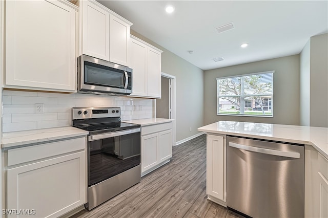 kitchen featuring light stone countertops, light wood-type flooring, tasteful backsplash, stainless steel appliances, and white cabinets