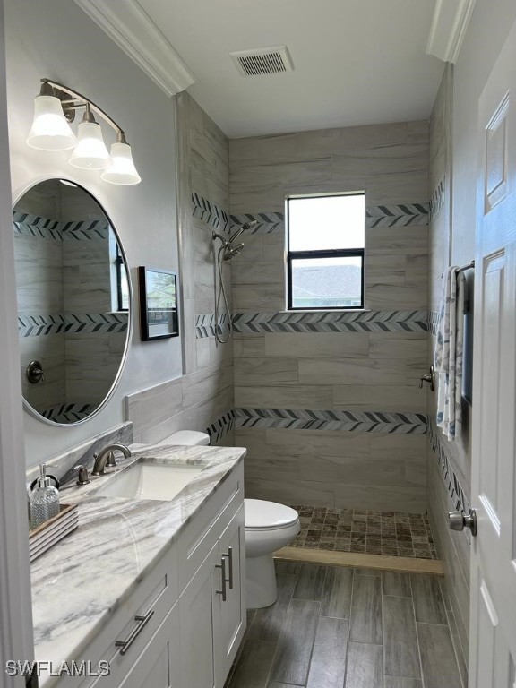 bathroom with a tile shower, crown molding, hardwood / wood-style floors, toilet, and vanity