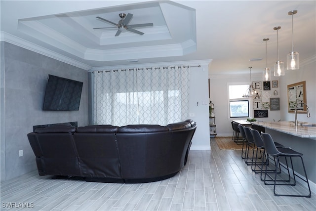 living room with ceiling fan, sink, a raised ceiling, crown molding, and light hardwood / wood-style floors