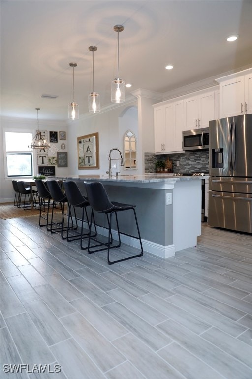 kitchen featuring white cabinetry, stainless steel appliances, hanging light fixtures, and light hardwood / wood-style flooring