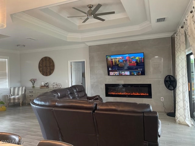 living room featuring a tray ceiling, ceiling fan, a fireplace, and light hardwood / wood-style flooring