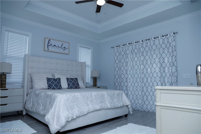 bedroom with wood-type flooring, a raised ceiling, ceiling fan, and ornamental molding