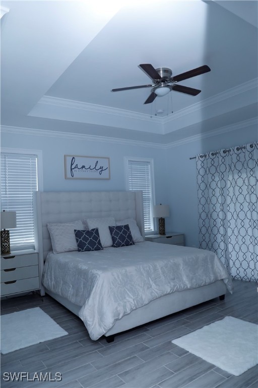 bedroom featuring wood-type flooring, a raised ceiling, ceiling fan, and ornamental molding