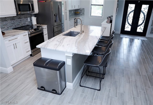 kitchen with a breakfast bar area, a kitchen island with sink, white cabinets, and stainless steel appliances